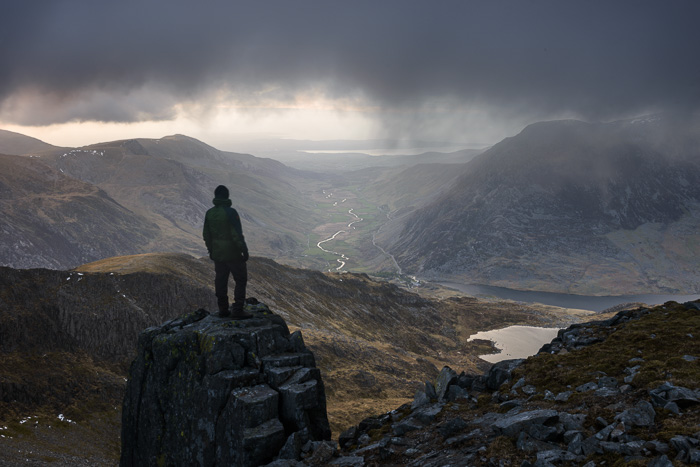 A male hiker admiring a view of the River Ogwen snaking through a valley in Snowdonia.